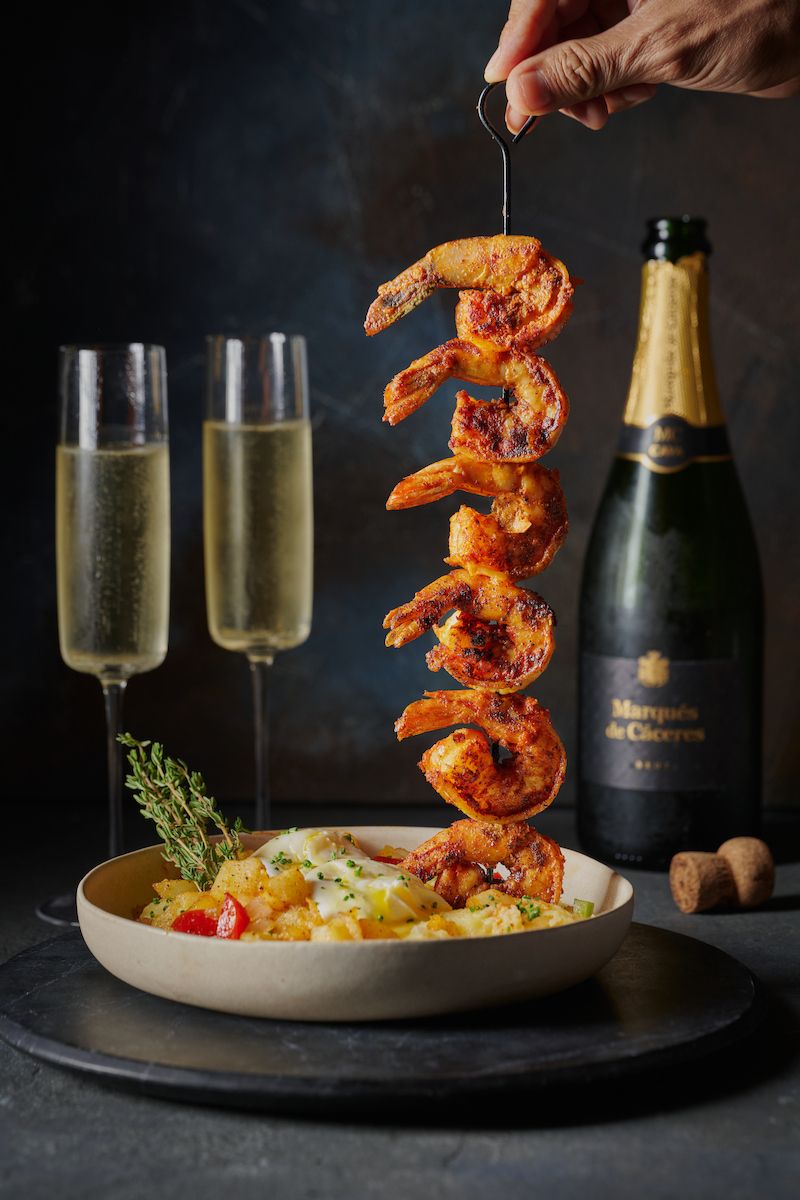 Skewered shrimp suspended over a bowl with champagne