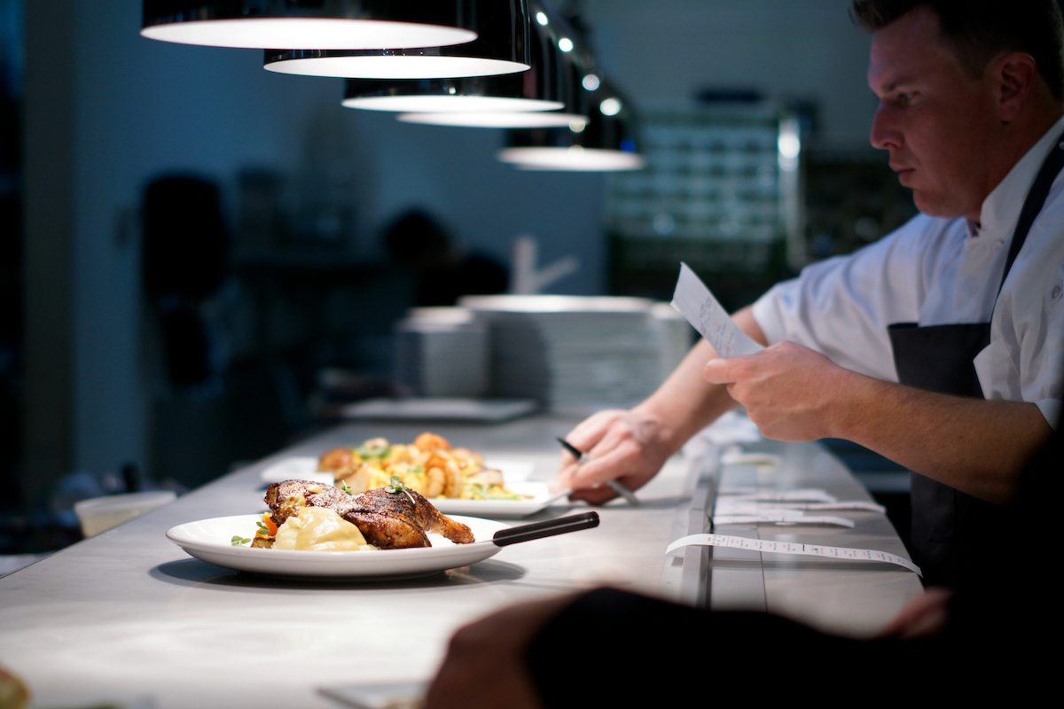 Chef plating at the pass under task lighting