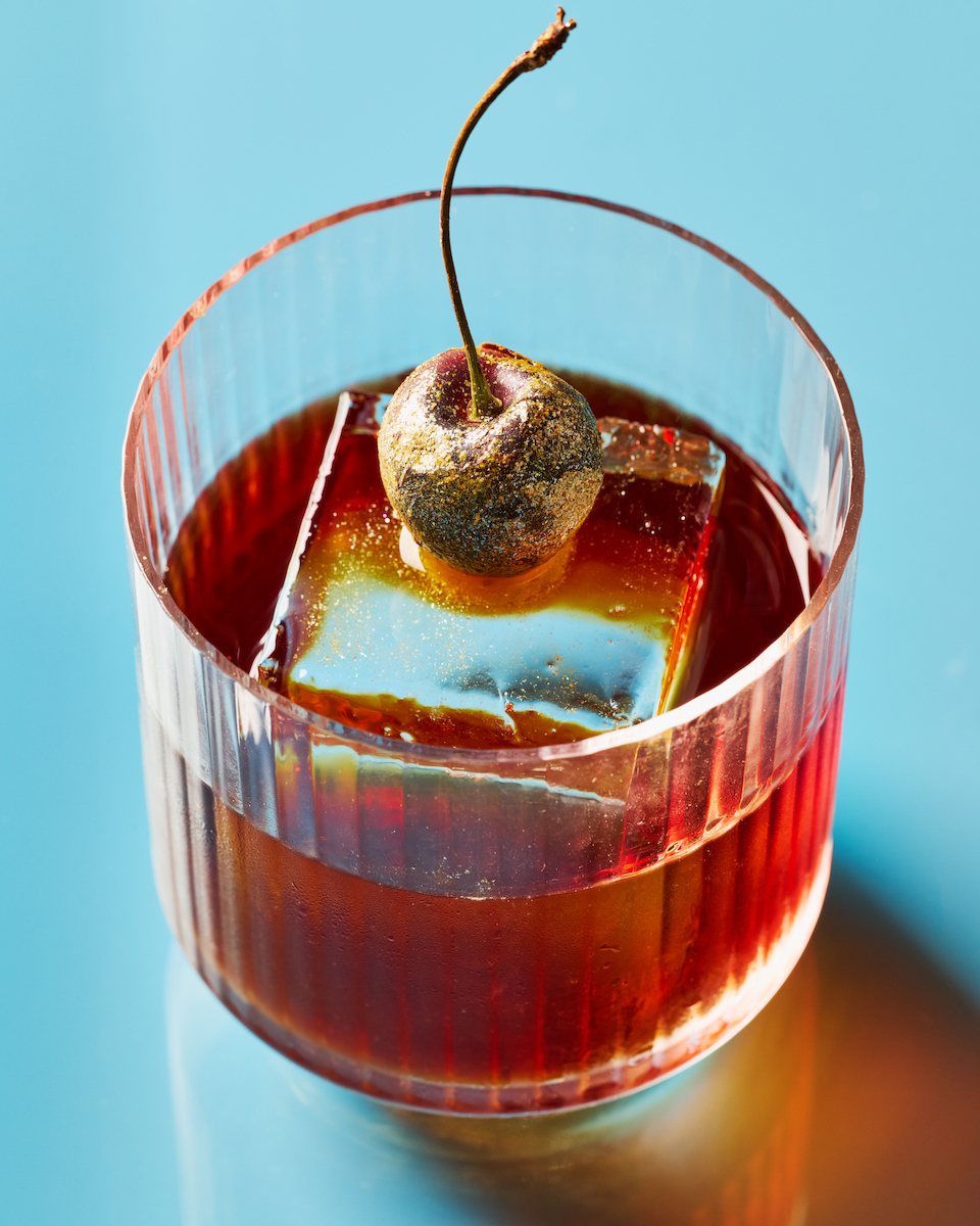 Old fashioned cocktail with gold-dusted cherry on blue